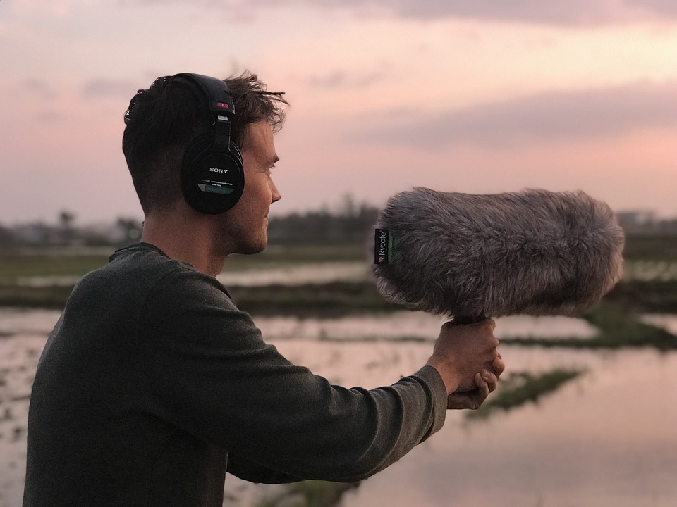 Man wearing headphones and holding a shotgun microphone in the wetlands.