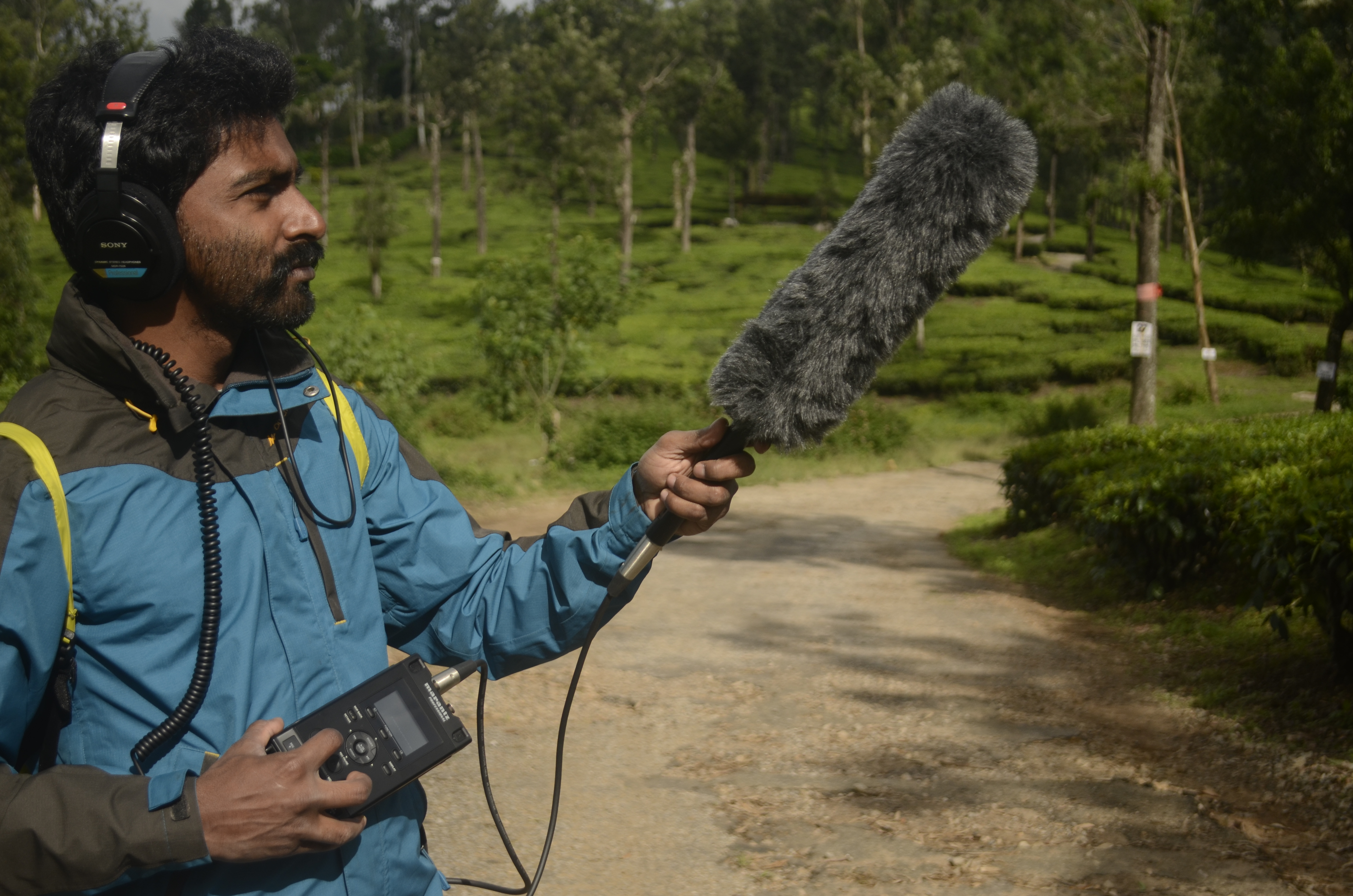 Man on a trail, wearing headphones and holding a microphone.