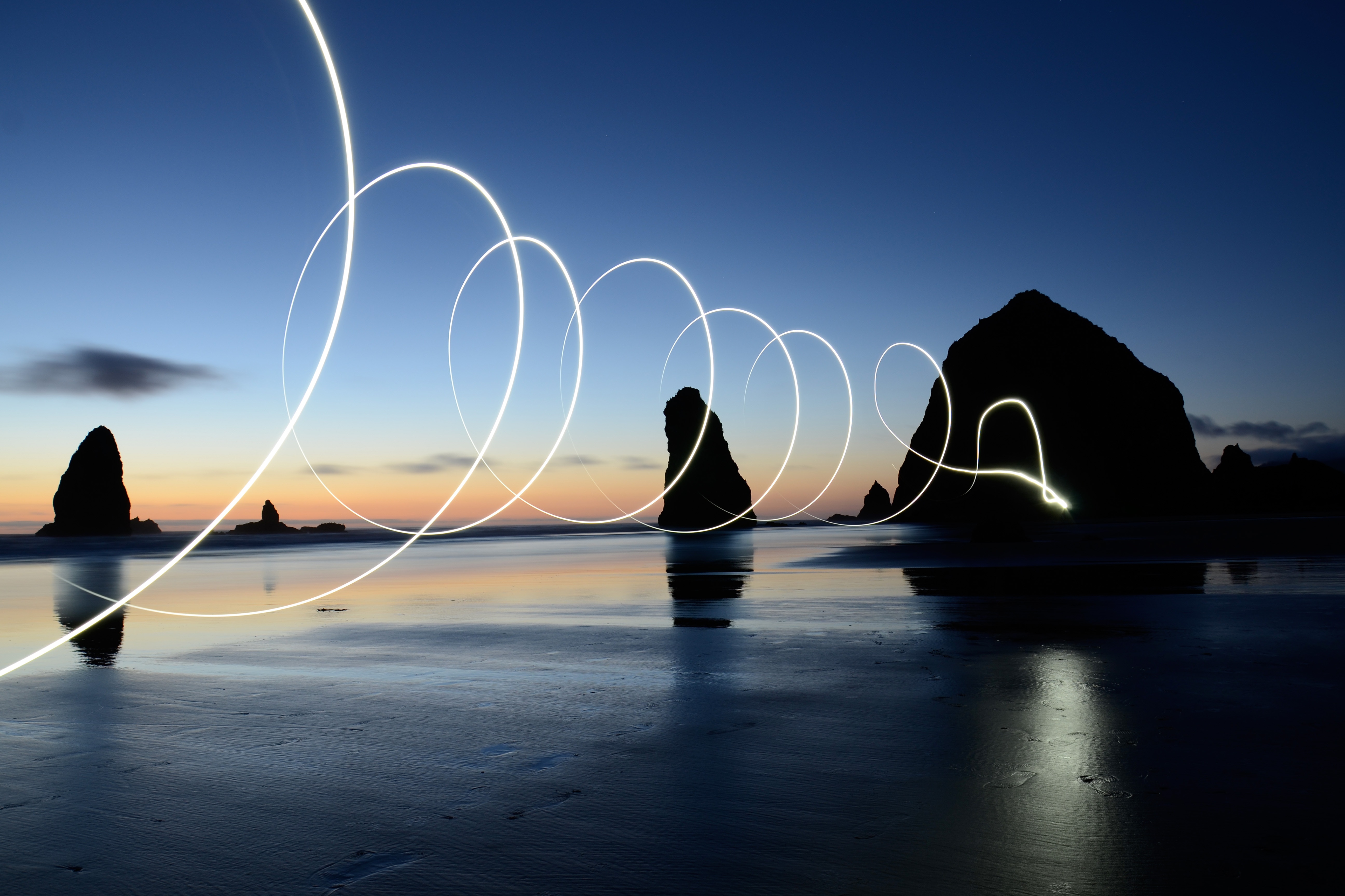 Calm beach at sunset with supernatural spirals of light emanating from a sea boulder.